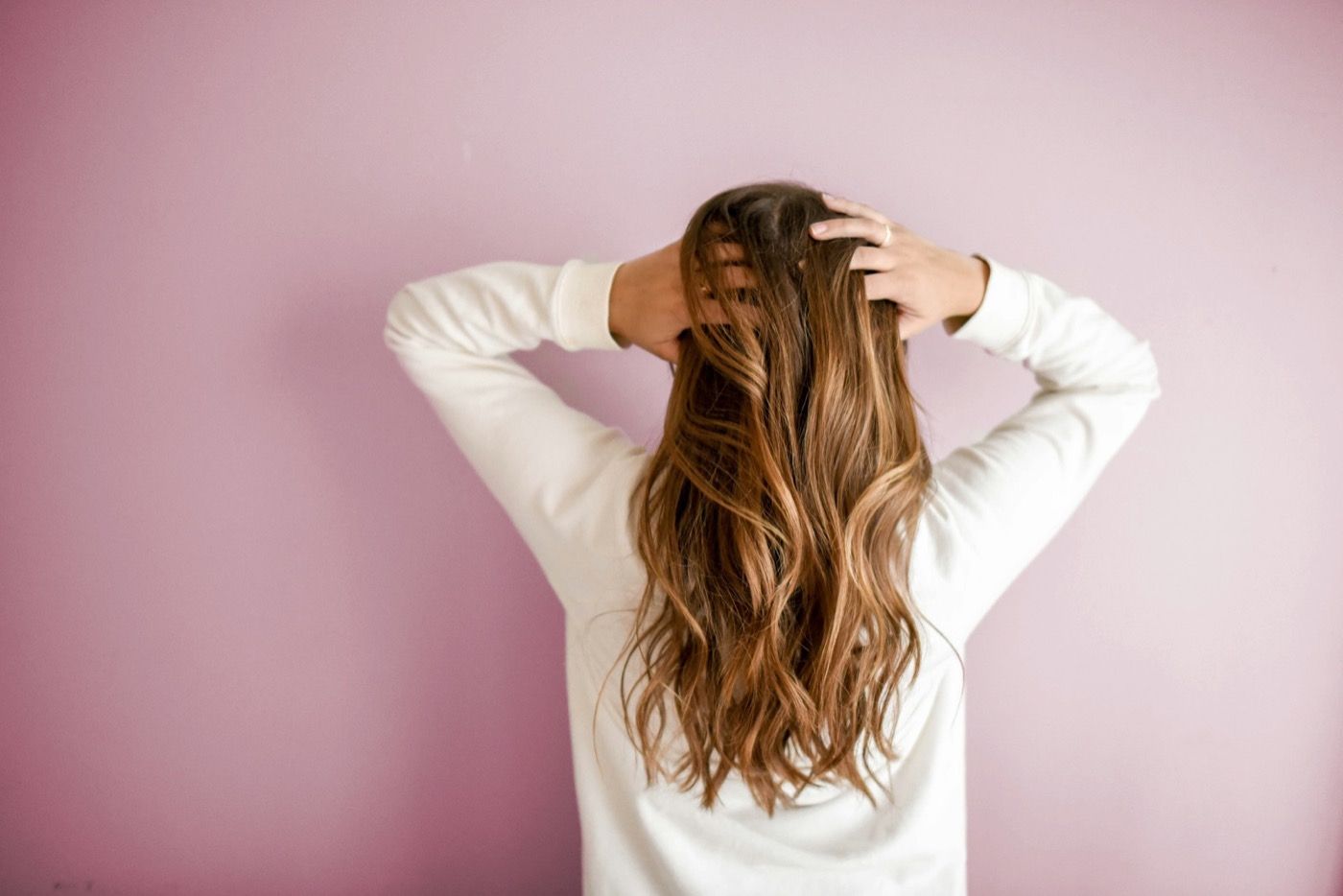 A woman seen from behind runs her hands through long wavy hair after a blow-dry.