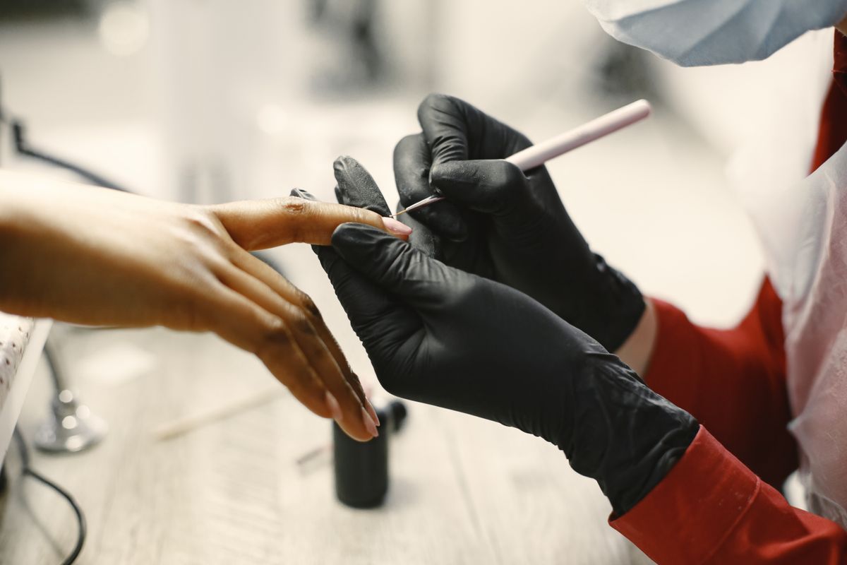 Una técnica en uñas con guantes aplica esmalte a una clienta.